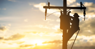 Uma silhueta de um homem trabalhando em um poste de energia elétrica, representando o mercado de utilities.
