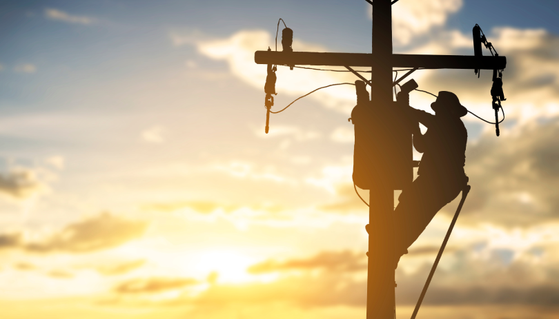 Uma silhueta de um homem trabalhando em um poste de energia elétrica, representando o mercado de utilities.