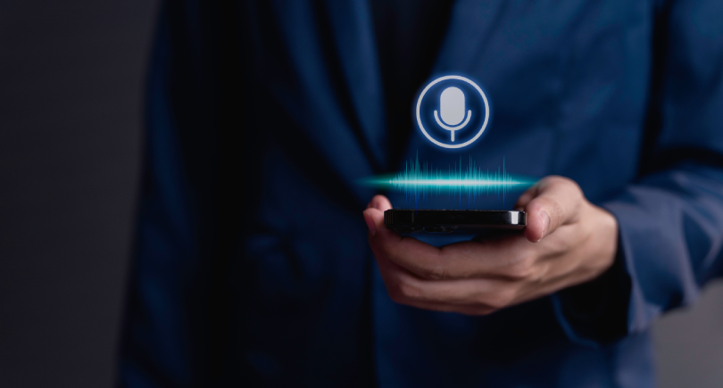 Um homem de terno azul segurando um telefone celular, que representa a captação de áudio para a transcrição em texto - API Speech-to-Text.