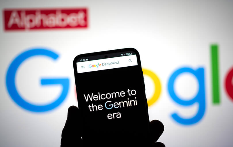 Gemini IA - Uma pessoa segurando um celular em frente ao logotipo do Google.