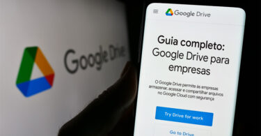 Close de uma pessoa segurando um celular. Na tela do celular, está a interface do Google Drive com o texto "Guia Completo: Google Drive para empresas".